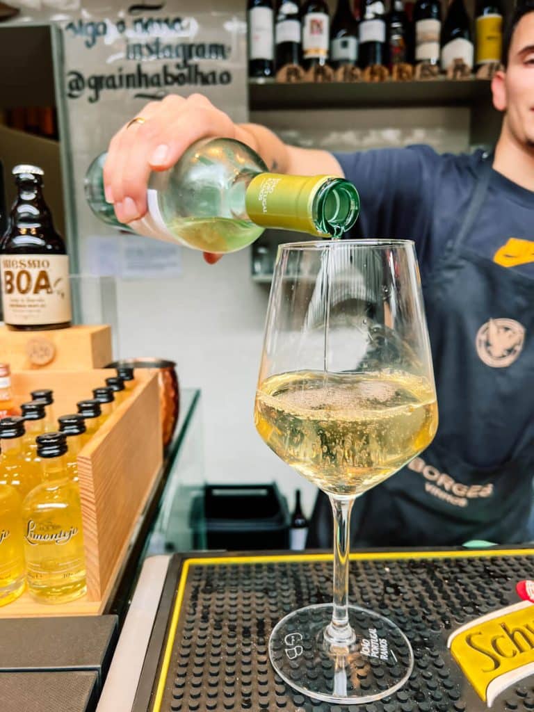 Vendor pouring a glass of vinho verde at Mercado do Bolhão in Porto, Portugal