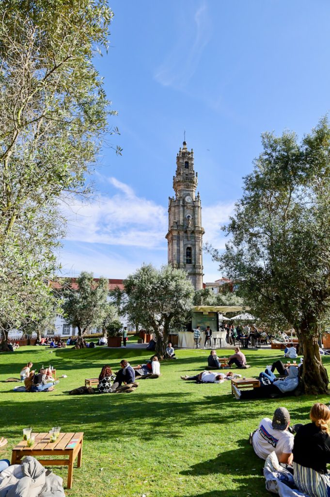 Small groups of people spread out in the grassy park below Clerigos Tower in Porto, Portugal