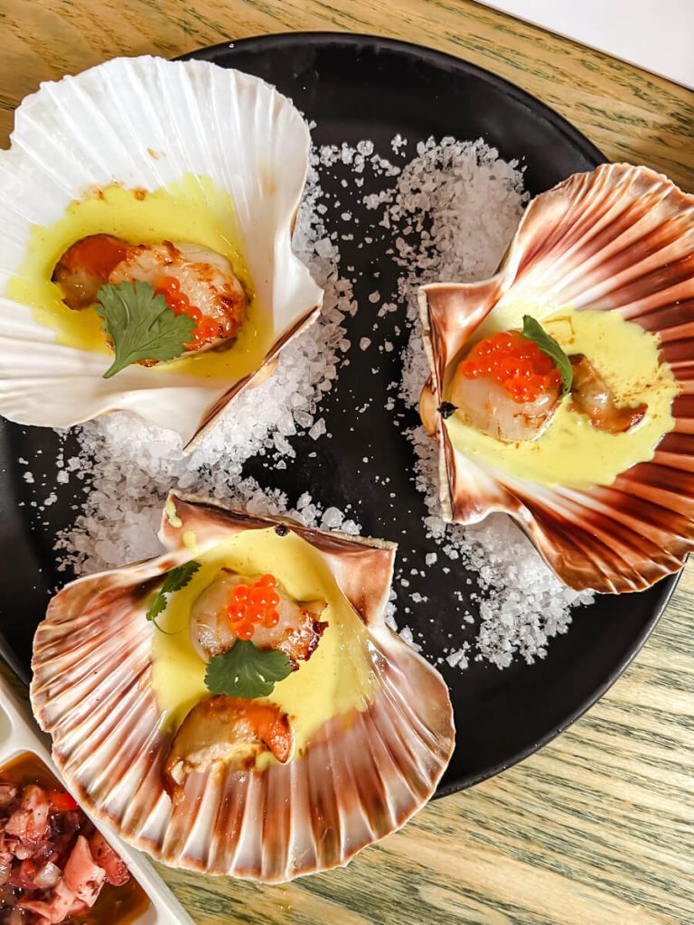 Scallop with caviar and saffron sauce plated inside a seashell