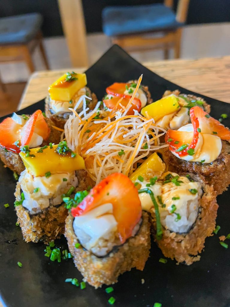 Plate of sushi rolls topped with mango and strawberry slices